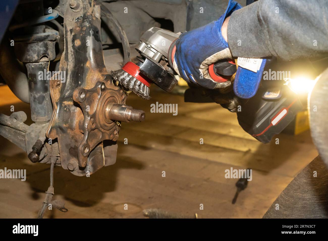 Der Automechaniker reinigt, entrostet und wartet das Radnabenlager. Gelbes Licht. Schutzhandschuhe. Stockfoto