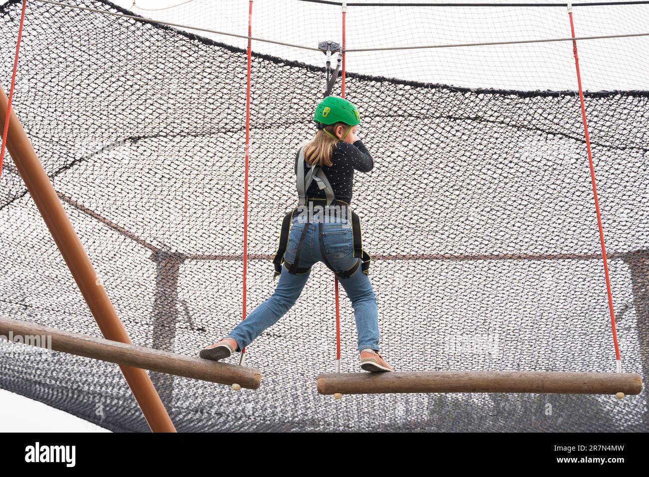Teenager-Mädchen mit Klettergeschirr-Ausrüstung, grüner Sport-Schutzhelm. Seilpark. Befestigung Karabiner an Sicherheitsseil. Hang Stockfoto
