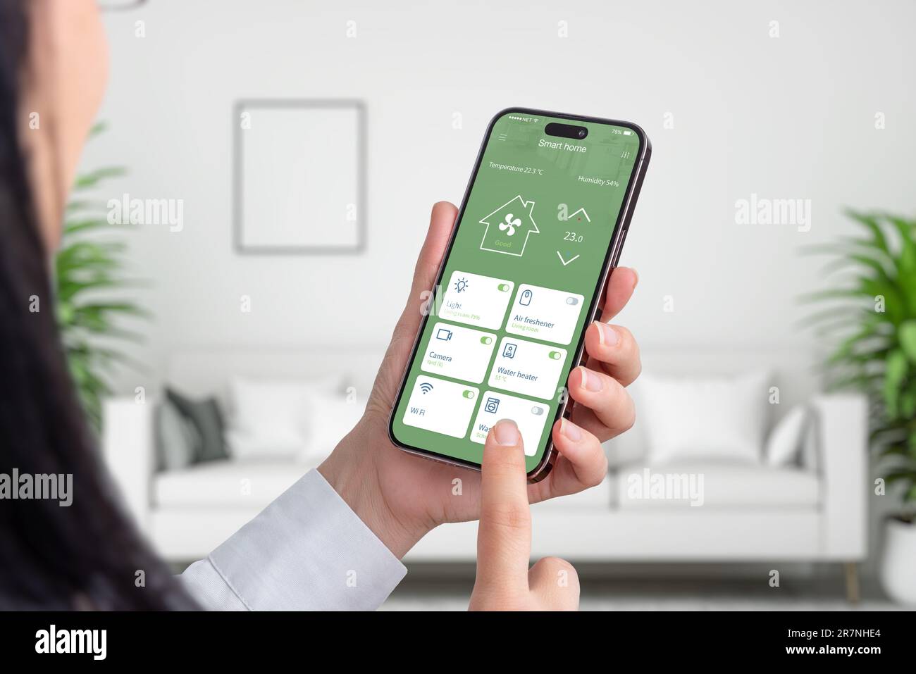 Frau verwendet Smart-Home-App auf Smartphone. Wohnzimmereinrichtung im Hintergrund. Hausautomatisierungskonzept Stockfoto