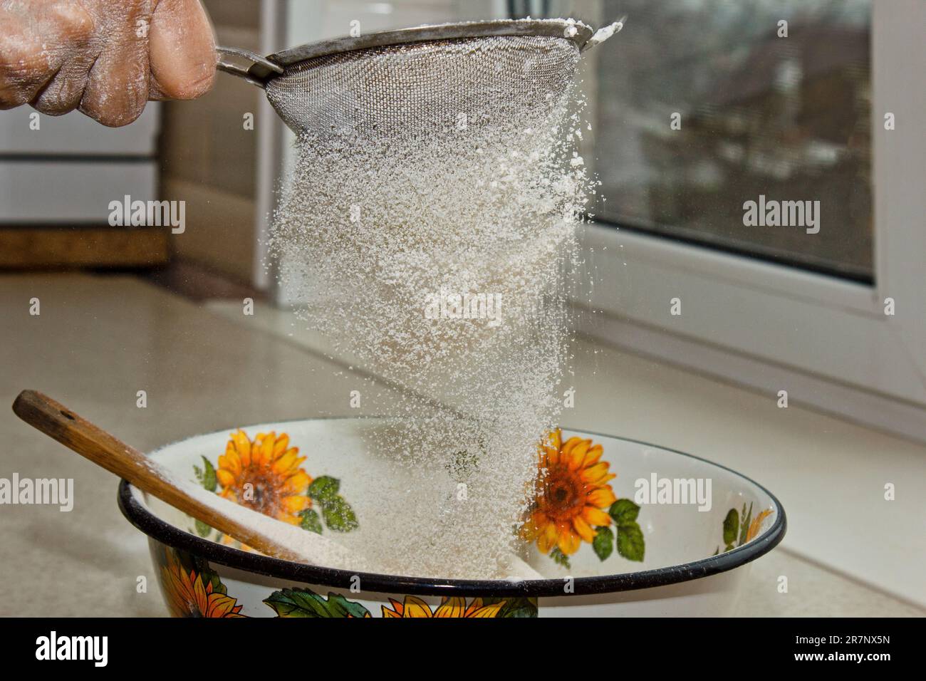 Weibliches Mehl, das von Hand durch ein manuelles Mehlsieb in einer Schüssel gesiebt wird, Nahkopie. Ich koche Teig. Küchengerät aus Metall. Stockfoto