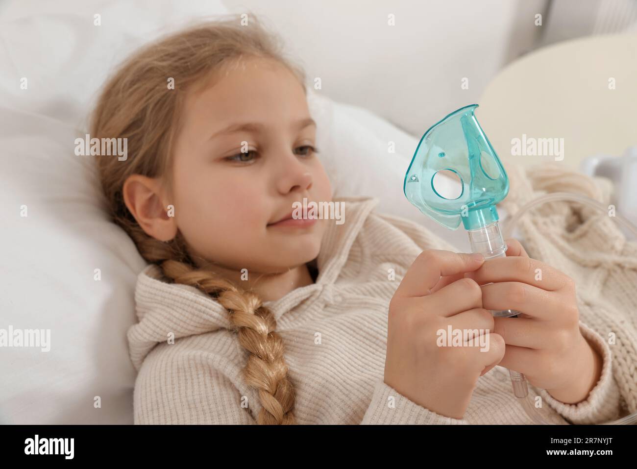 Kleines Mädchen, das den Vernebler zur Inhalation auf dem Bett zu Hause hält Stockfoto