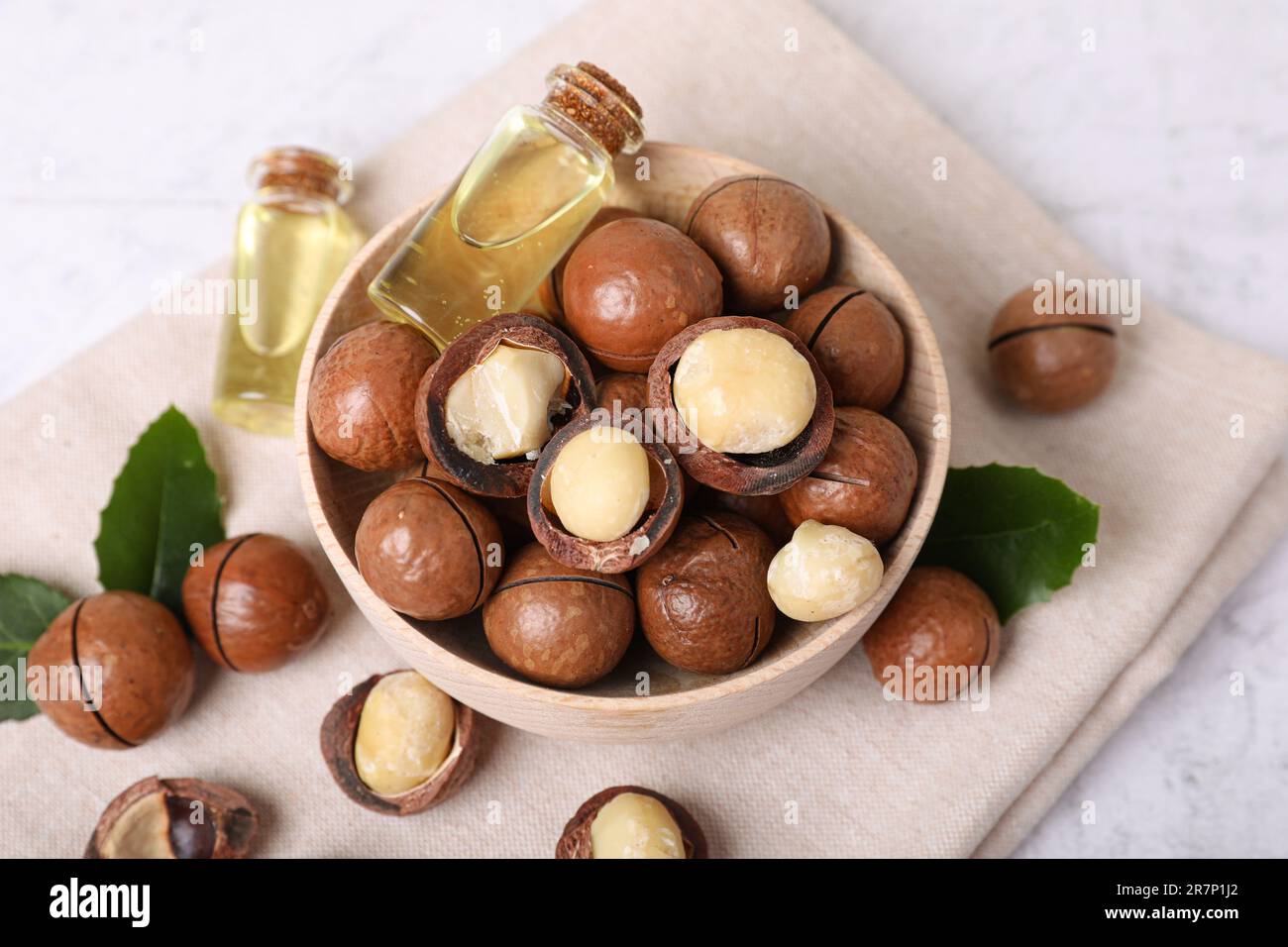 Schüssel mit Bio-Macadamia-Nüssen und natürlichem Öl auf weißem, strukturiertem Tisch, Ansicht oben Stockfoto