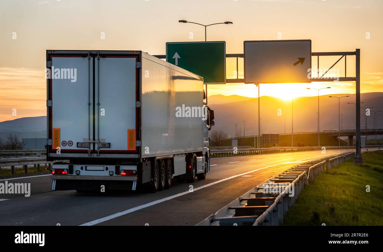 Großer weißer Frachtwaggon, der auf der Straße unterwegs ist, mit Sonnenuntergangslandschaft, schneller Lieferung, Frachtlogistik und Frachtversandkonzept Stockfoto