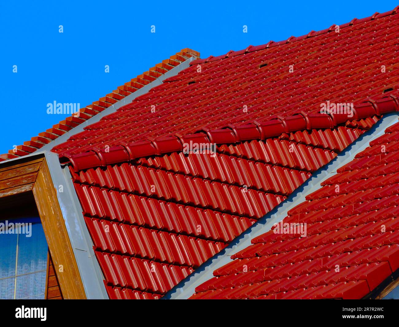 Geneigtes Wohndach. Rote Tonfliesen und Metallblitze. Blauer Himmel. Helles Sonnenlicht. Baugewerbe. Hausbesitzkonzept. Freundliches Haus-Design Stockfoto