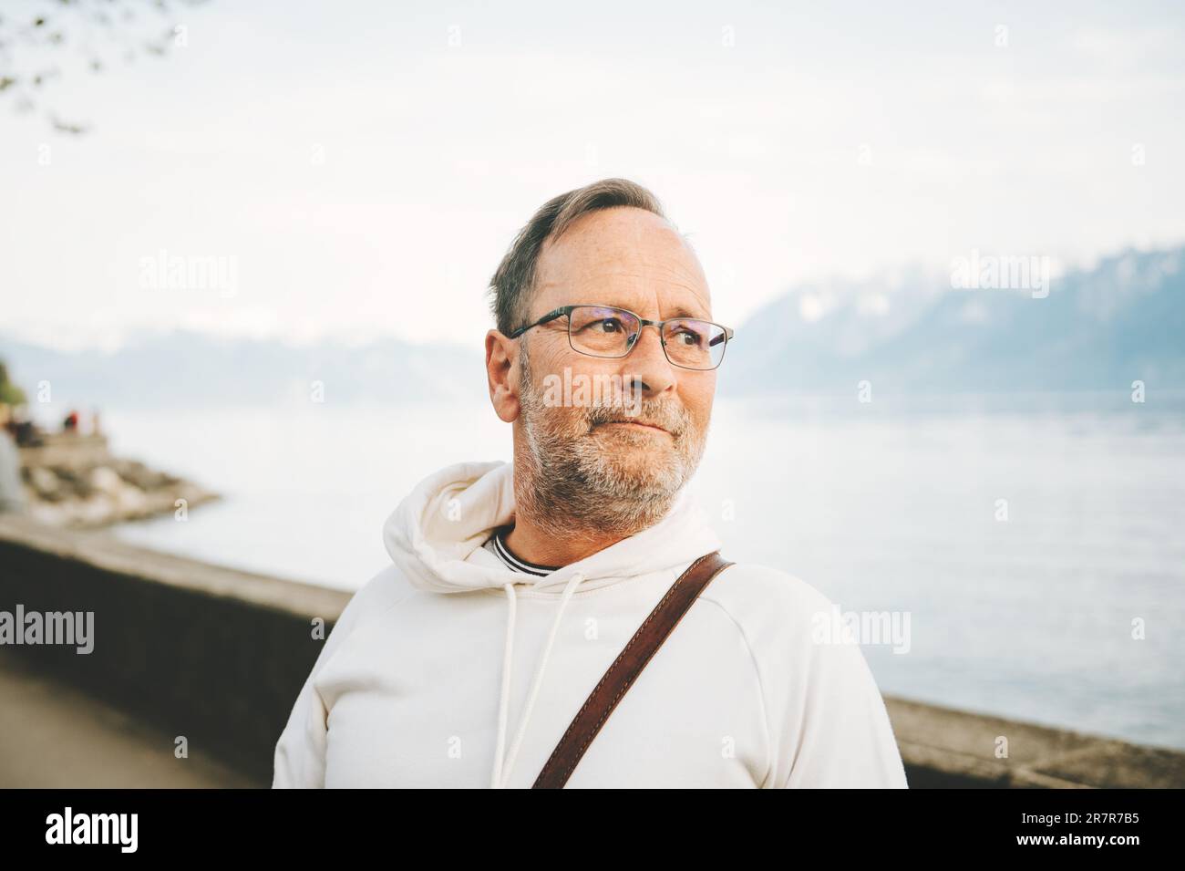 Portrait eines gutaussehenden Mannes, der einen wunderschönen See mit Bergen bewundert, mit weißem Sweatshirt Stockfoto