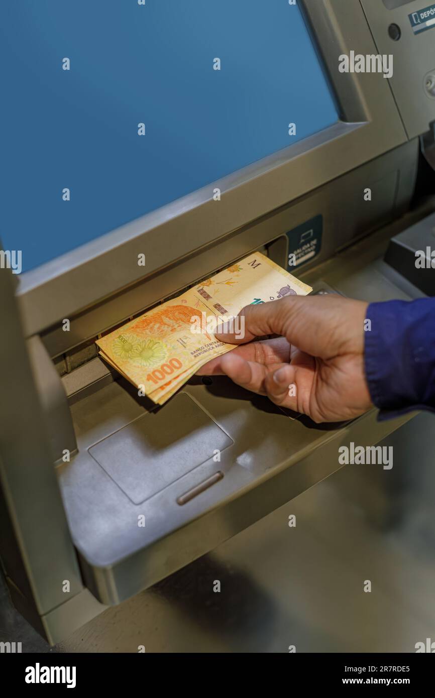 Detail einer Männerhand, die argentinische Pesos aus einem Geldautomaten extrahiert. Stockfoto