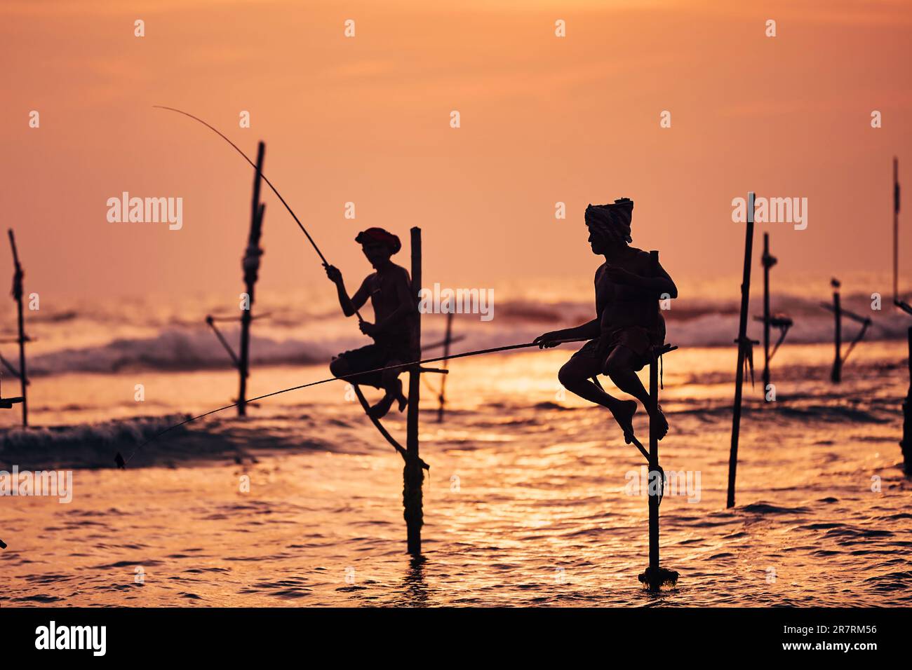 Silhouetten zweier traditioneller Fischer gegen das Meer in der Dämmerung. Traditionelles Pfahlfischen in der Nähe von Galle in Sri Lanka. Stockfoto