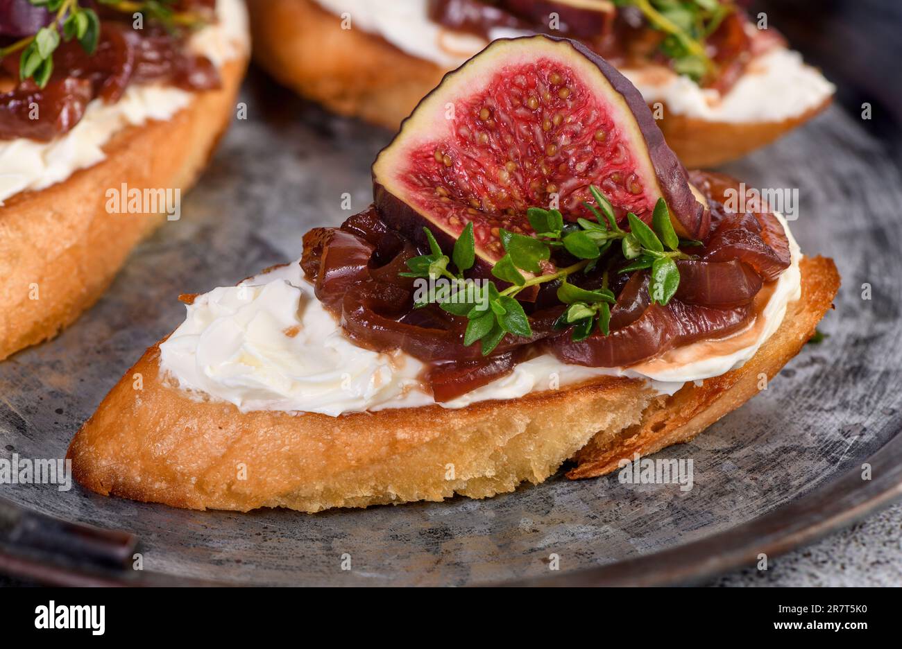 Cannapé oder Crostini mit geröstetem Baguette, Frischkäse, Zwiebelmarmelade, Feigen und frischem Thymian auf einer Dose. Ideale Vorspeise als Aperitif. Stockfoto