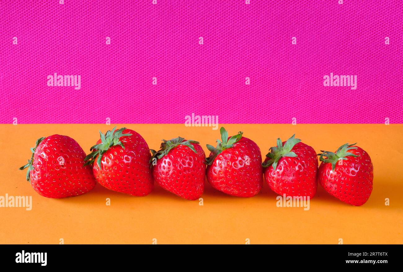 Eine Reihe frischer Erdbeeren auf einem lebhaften farbigen Hintergrund, kostenloser Kopierraum, Obst, gesunde Lebensmittel, Sommerkonzept. Stockfoto