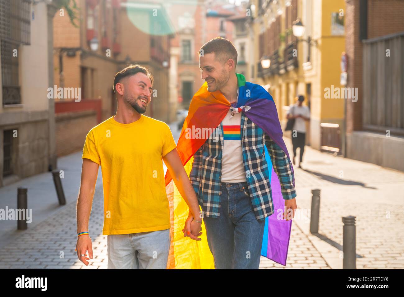 Homosexuelle Männer, die auf einer Party in der Stadt mit einer Regenbogenflagge lächelnd spazieren, lgbt Concept Stockfoto