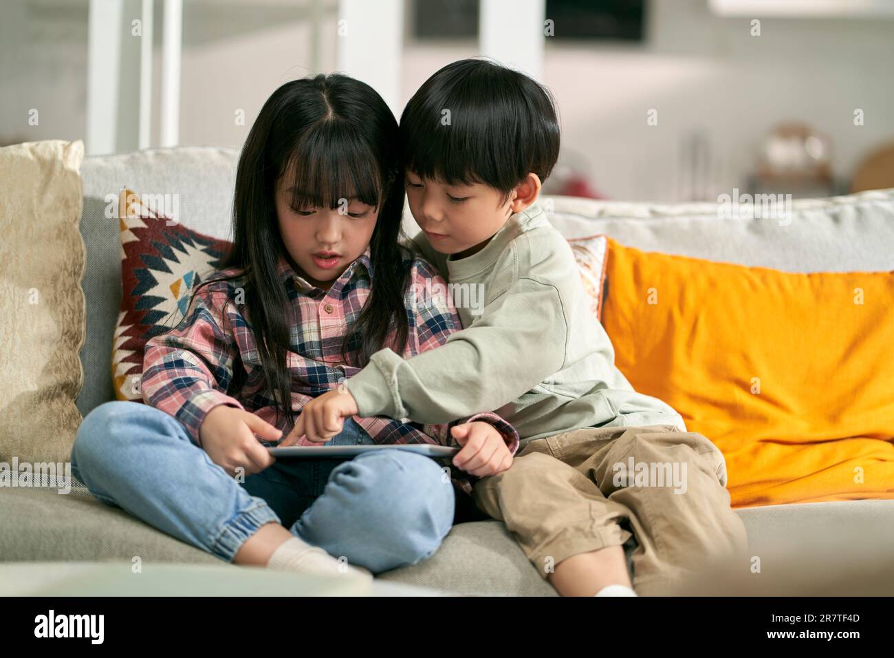 Kleine asiatische Kinder, Bruder und Schwester, die zu Hause auf dem Familientisch sitzen und einen digitalen Tablet-Computer benutzen Stockfoto