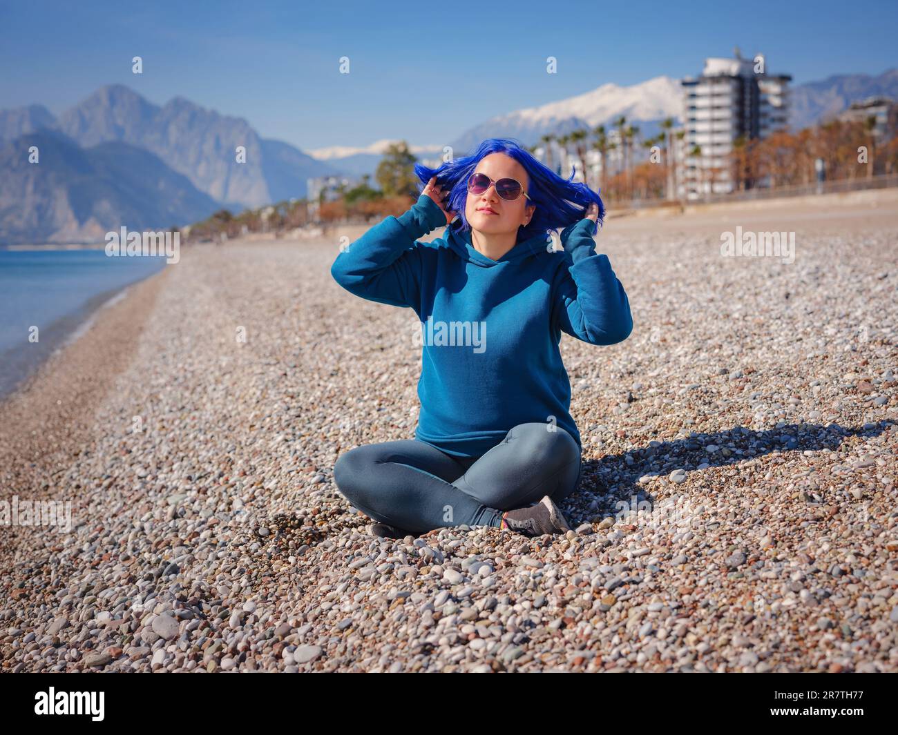 Eine Frau trägt einen hellblauen Hoodie und Jeans in Übergröße. Blauhaarige Frau draußen im Park am Strand von Antalya. Kleidungsmodell, leerer Platz für Text o Design. Stockfoto
