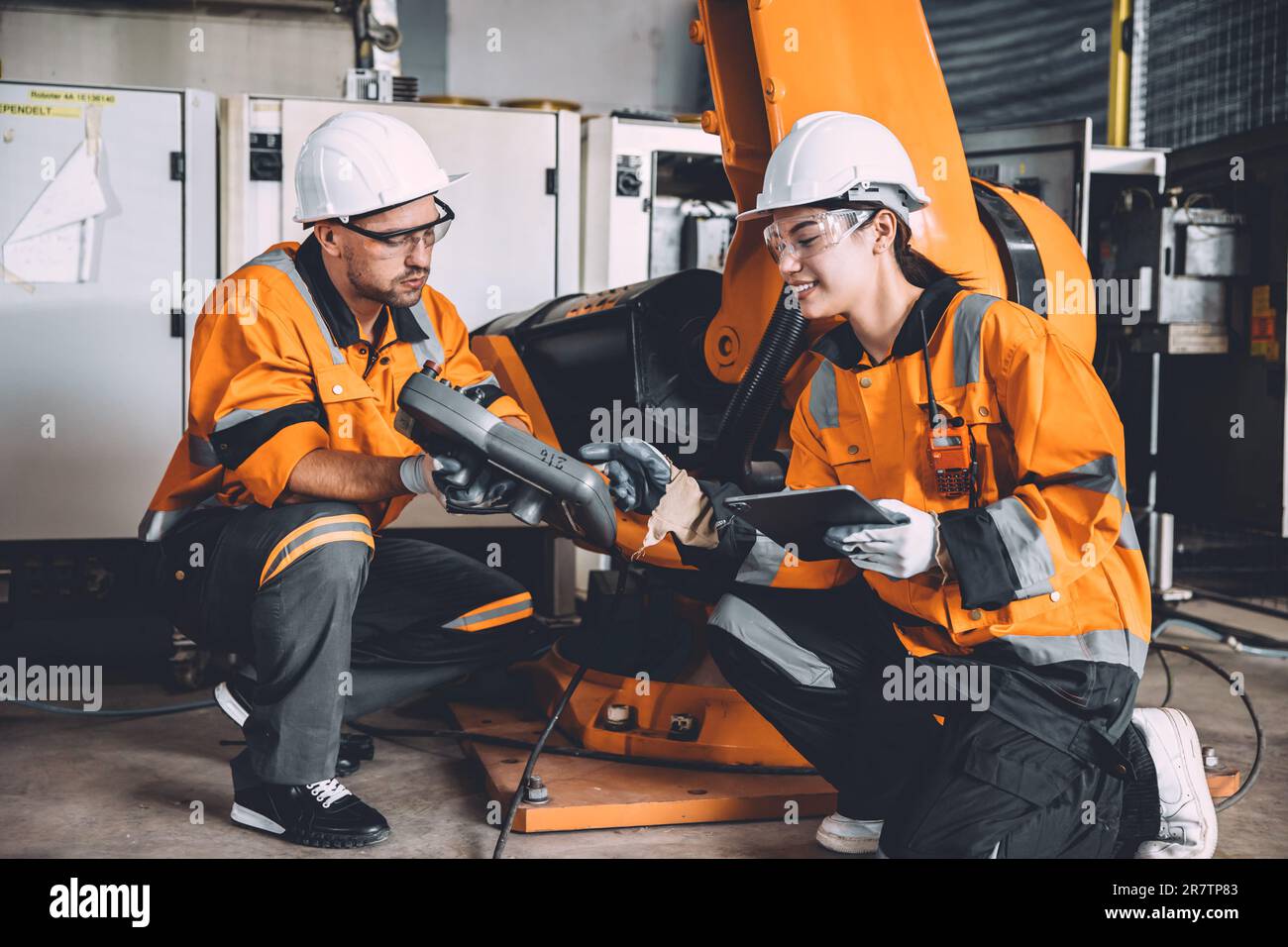Ingenieurteam, das zusammenarbeitet, um neue Mitarbeiter für die Bedienung von Handsteuerungsroboterarm-Schweißgeräten in der Schwerindustrie in Automatisierungsfabriken zu Schulen. Stockfoto