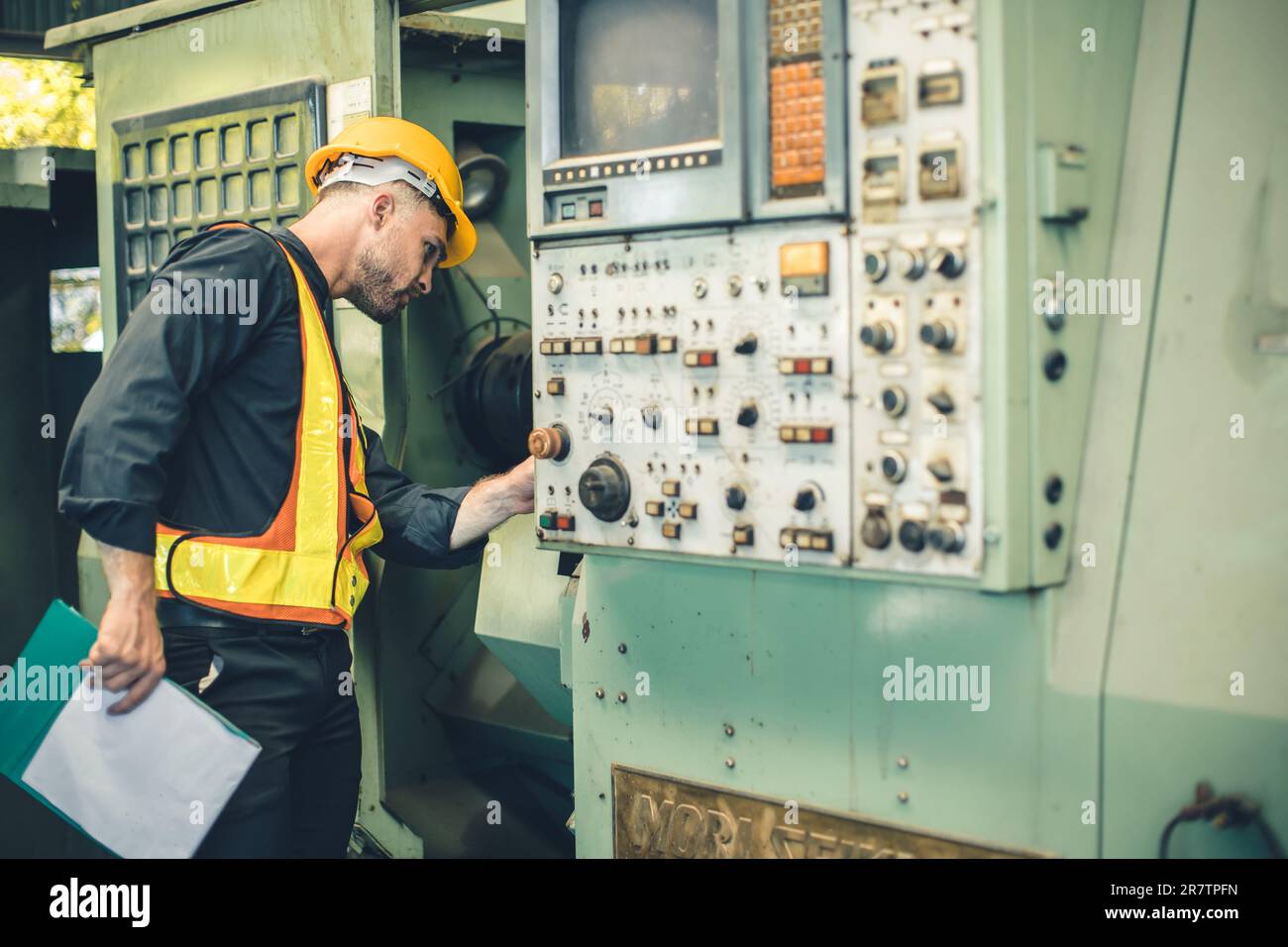 Junger Ingenieur, männlicher Arbeiter, Scheckdienst, alte CNC-Drehmaschine in der Schwermetallindustrie Stockfoto