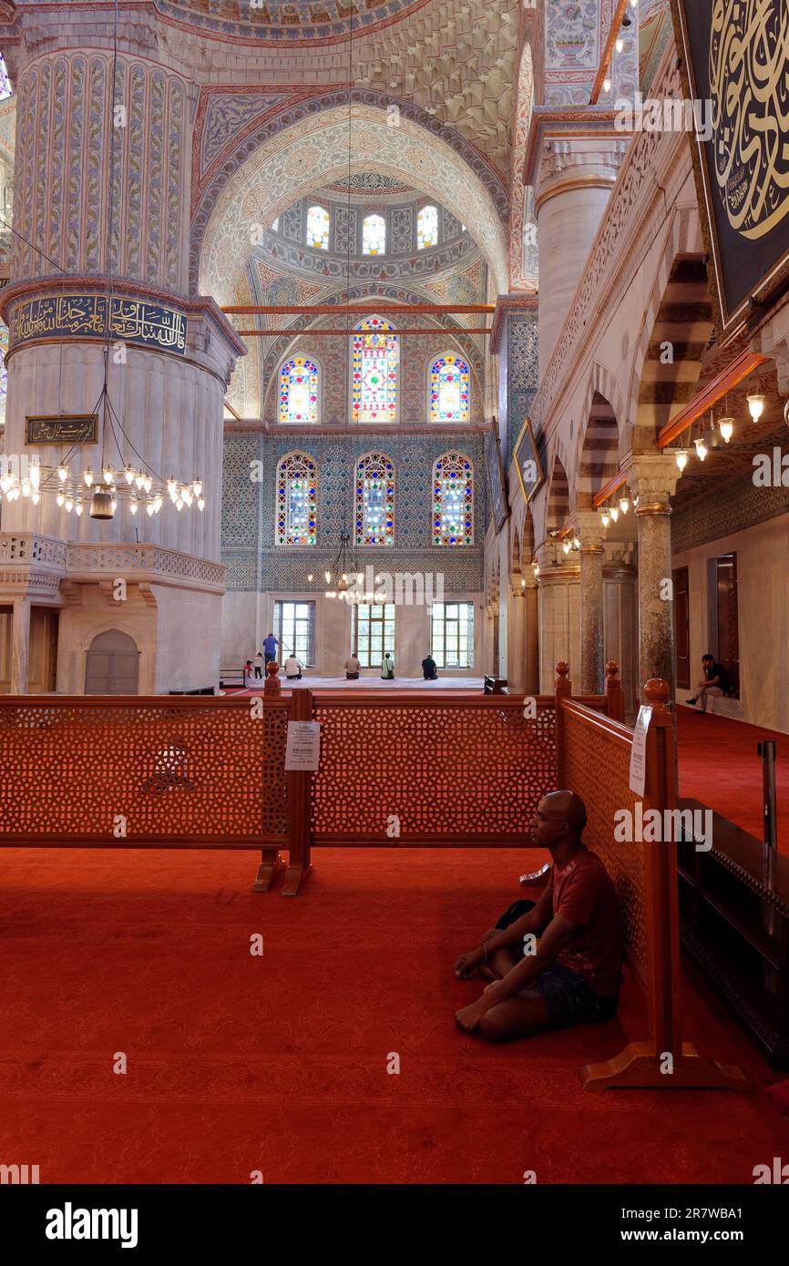Der Mensch sitzt und meditiert oder betet allein in der Blauen Moschee alias Sultan Ahmed Moschee, während andere Männer an der Front beten, Istanbul, Türkei Stockfoto