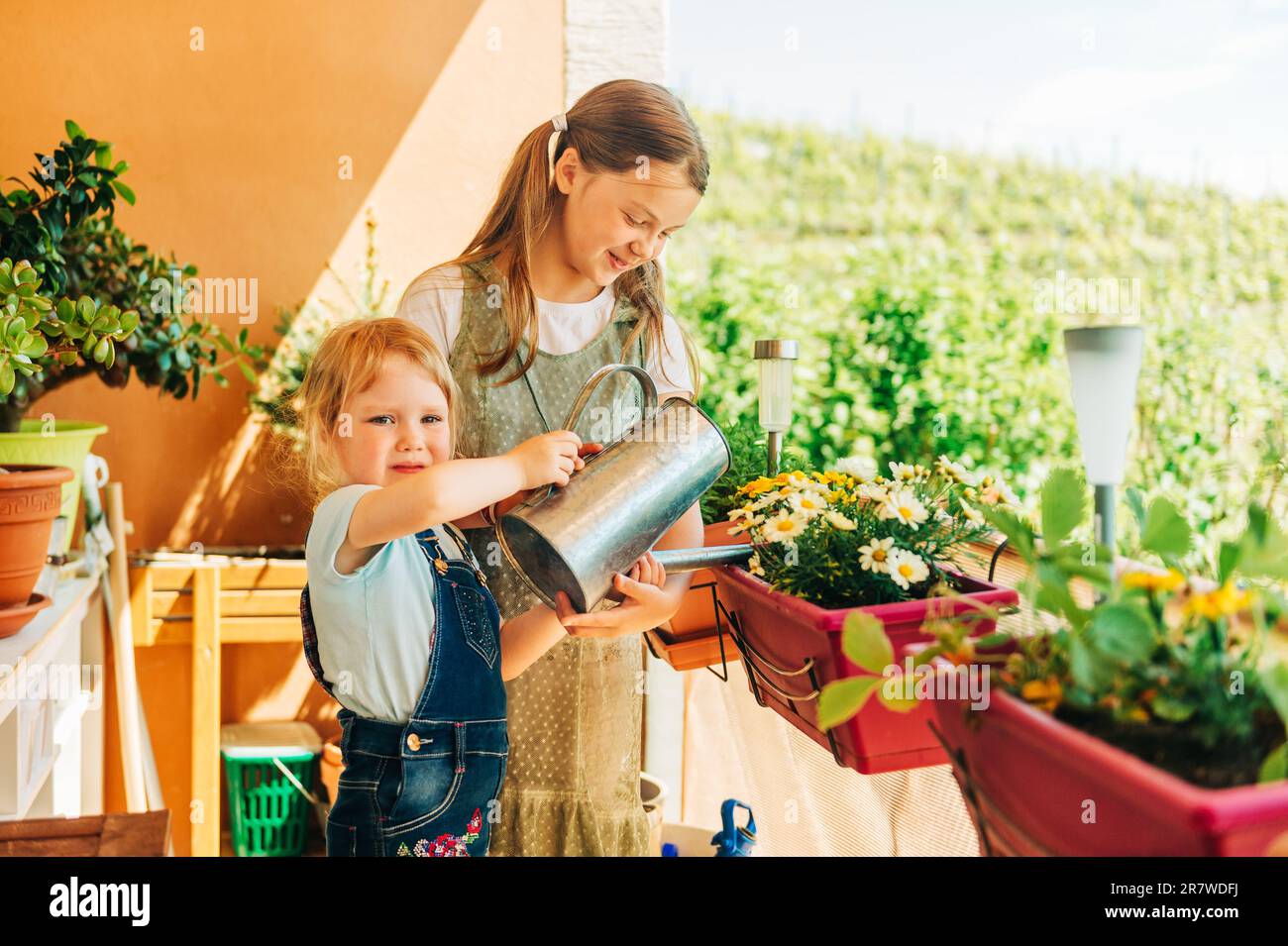 Gruppe von zwei Kindern, die Blumen auf dem Balkon gießen, ein kleines Mädchen hilft mit dem kleinen Garten Stockfoto