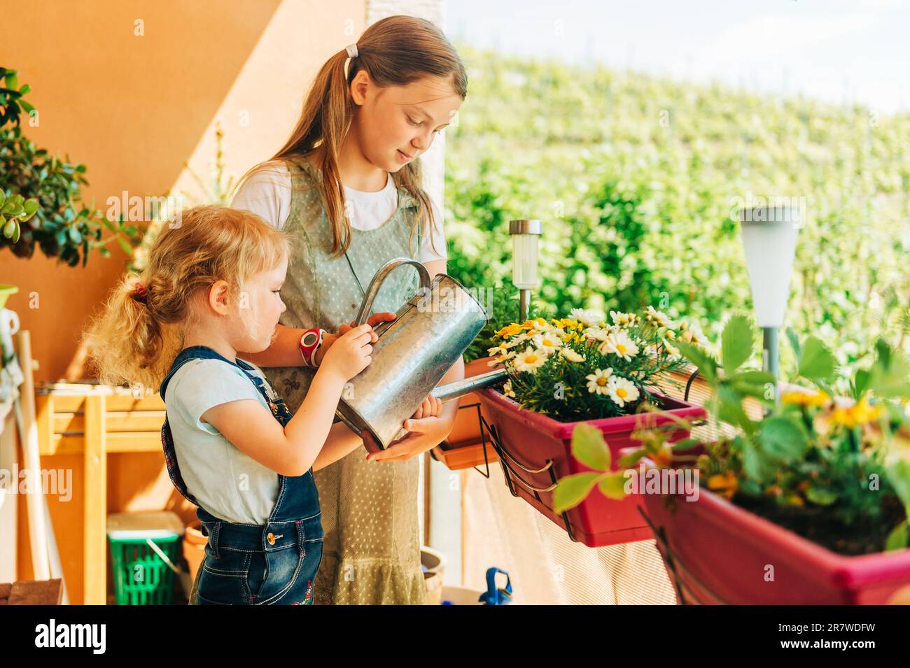 Gruppe von zwei Kindern, die Blumen auf dem Balkon gießen, ein kleines Mädchen hilft mit dem kleinen Garten Stockfoto