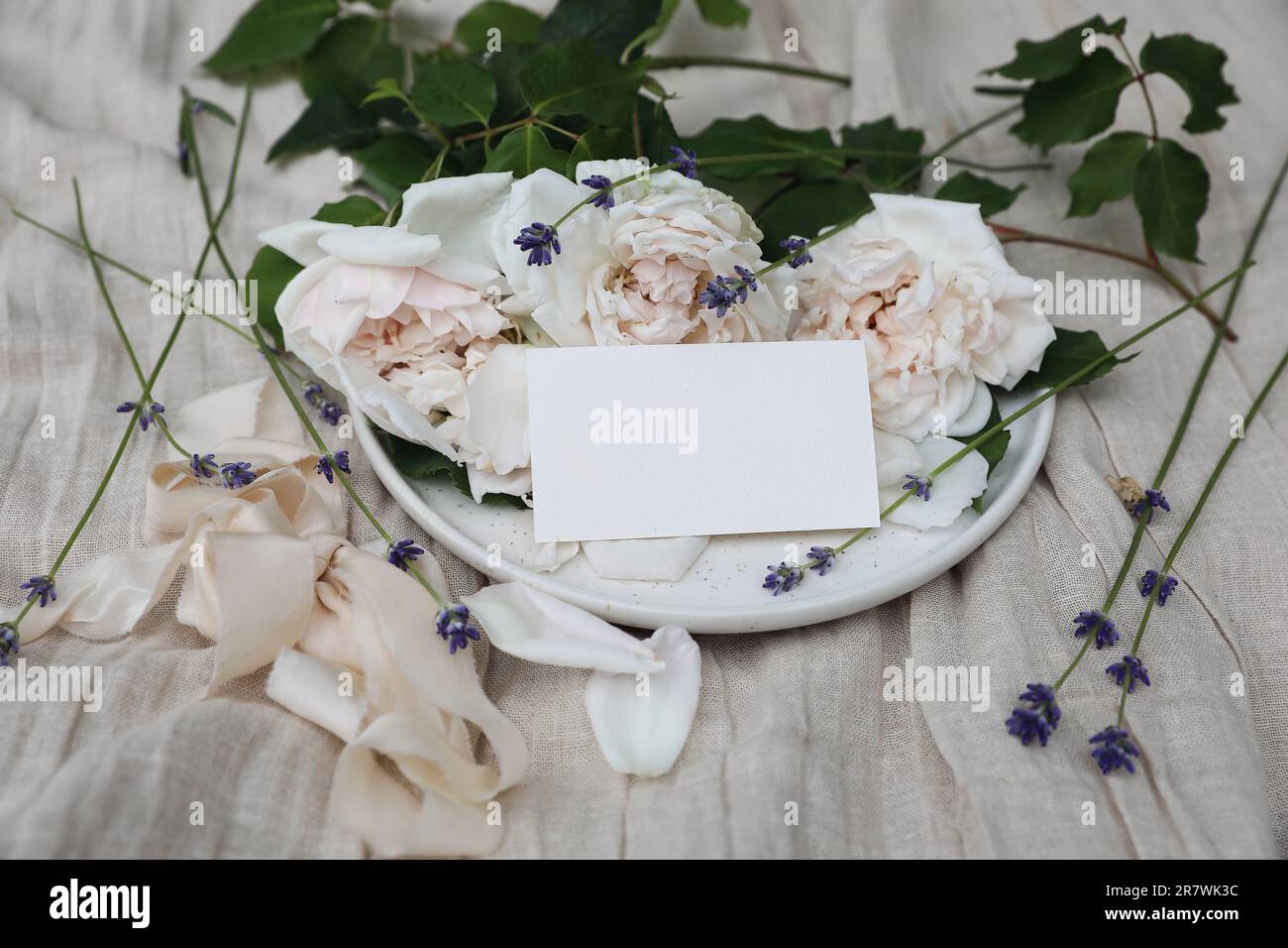 Festliche Blumenkomposition mit englischen Rosen, Lavendel, Band. Leere Visitenkarte, Hochzeitseinladungsmodell. Tischdecke aus beigefarbenem Leinen Stockfoto