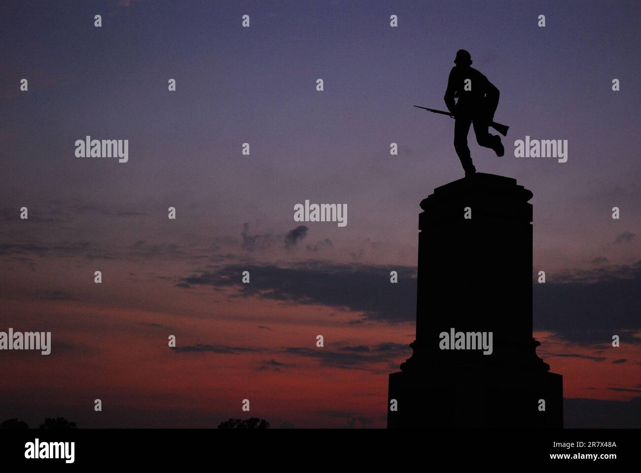 Das Minnesota Memorial zeigt einen Soldaten, der mit einem Gewehr bei Sonnenuntergang auf dem Gelände des Gettysburg National Battlefield angreift und läuft Stockfoto