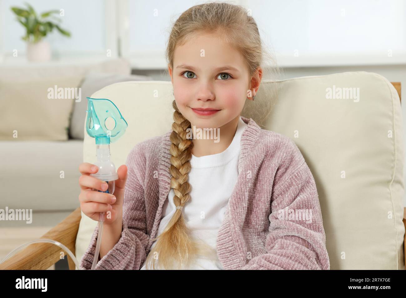 Kleines Mädchen hält Vernebler zur Inhalation im Sessel zu Hause Stockfoto