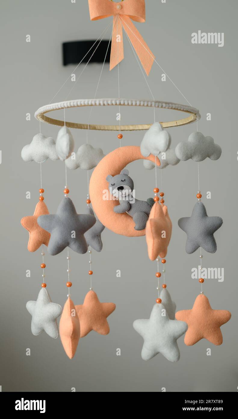 Kinderbett-Mobile hängt im Kinderzimmer, orangefarbenes und graues Pastellmotiv, schlafender Bär auf dem Mond umgeben von Sternen. Stockfoto