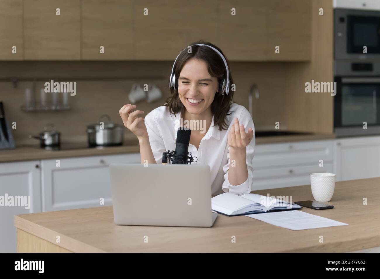 Weibliche Podcaster sitzt am Küchentisch und spricht ins Mikrofon Stockfoto