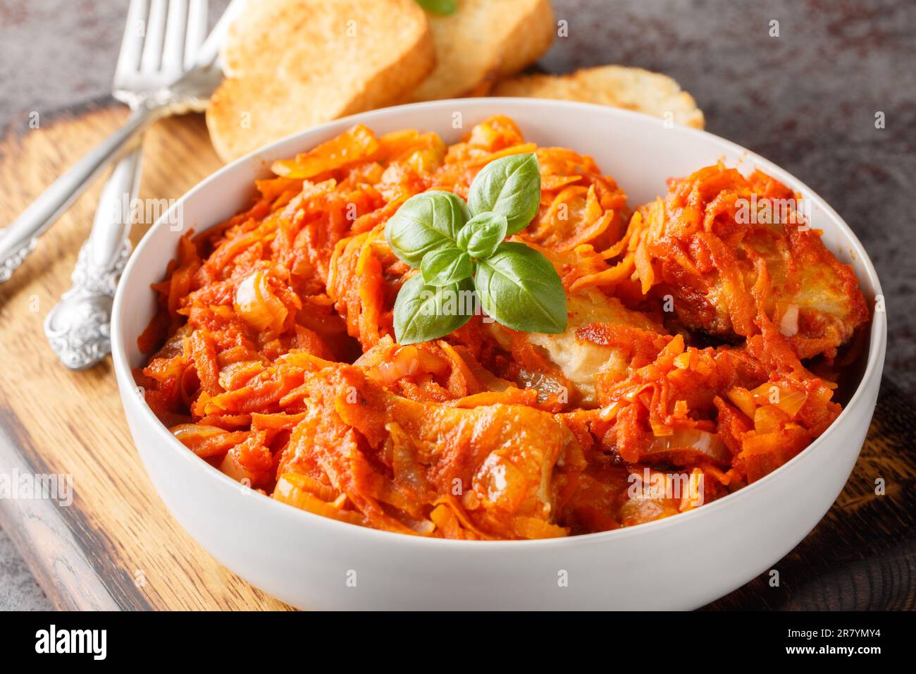 Stücke von weißem Meeresfisch mit Gemüse in Tomatensauce serviert mit Toast Nahaufnahme auf einem Holzbrett auf dem Tisch. Horizontal Stockfoto