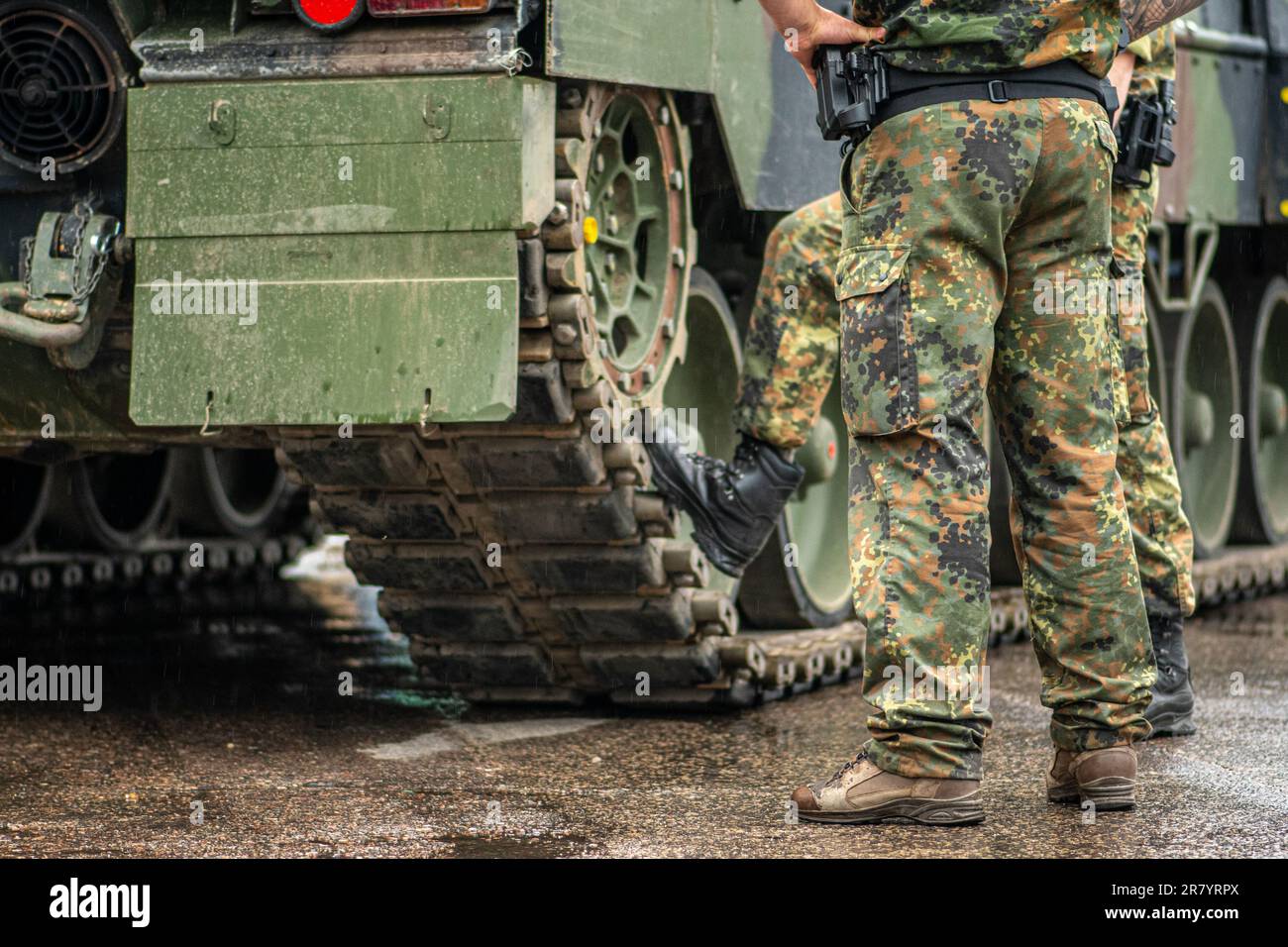 Zwei Soldaten in Tarnuniform standen während einer Pause unter dem Regen neben den Schienen eines gepanzerten Panzers, nur die Hosen und die Stiefel Stockfoto