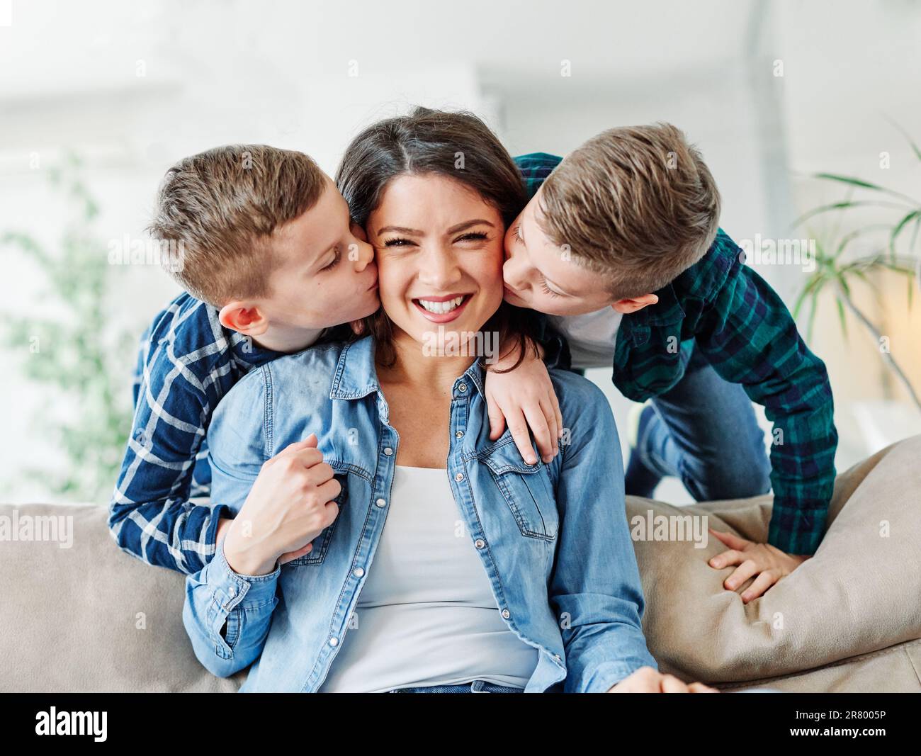 Aufnahme von zwei süßen kleinen Jungen, die ihre Mutter zu Hause liebevoll küssen Stockfoto
