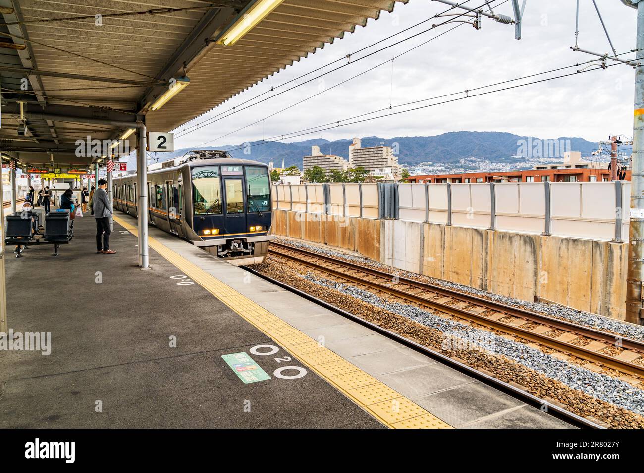 Die Insel-ähnliche Plattform des Bahnhofs Sakura Shukugawa in Nishinomiya, an der JR Kobe-Linie, mit einigen Leuten, die an einem bedeckten Tag warten. Stockfoto