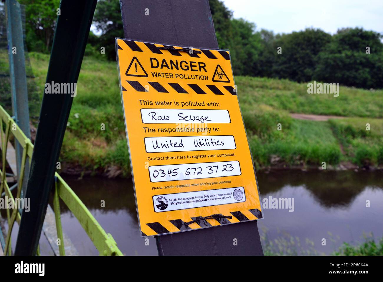 Manchester, Vereinigtes Königreich, 18. Juni 2023. In einer Protestmitteilung der Dirtywater-Kampagne auf der Jackson's Bridge über dem Fluss Mersey wird behauptet, dass der River Mersey, Sale Water Park, Großbritannien, durch rohes Abwasser verschmutzt ist, und behauptet, dass United Utilities (UU) dafür verantwortlich ist und eine Telefonnummer gibt, um eine Beschwerde einzureichen. Die Schmutzwasserkampagne scheint Teil der Rebellion zu sein, die ausgelöscht wurde. Im Februar berichtete die BBC, dass der nahe gelegene Stockport Council eine Untersuchung eingeleitet hatte, nachdem er festgestellt hatte, dass UU im Jahr 2022 977 Mal Abfall in den Fluss Mersey gebracht hatte. Kredit: Terry Waller/Alamy Live News Stockfoto