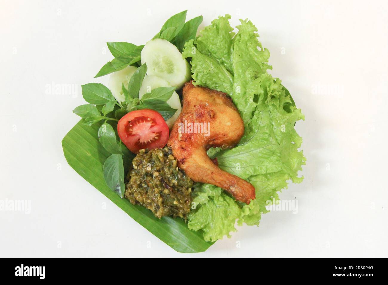 Galangal gebratenes Hähnchen, Sambal, Tomate, Gurke, Basilikum, Salat. Indonesische Küche auf Bananenblatt-Teller. Gastronomie-Fotografie auf weißem Hintergrund Stockfoto