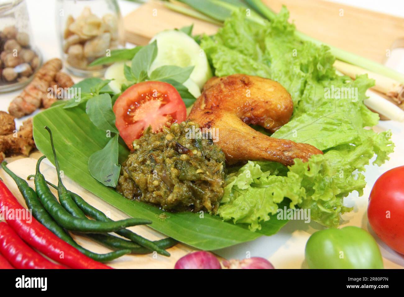 Galangal gebratenes Hähnchen, Sambal, Tomaten, Gurke, Basilikum, Salat. Indonesische Küche auf Bananenblatt-Teller. Gastronomie Fotografie und Zutaten Gewürze Stockfoto