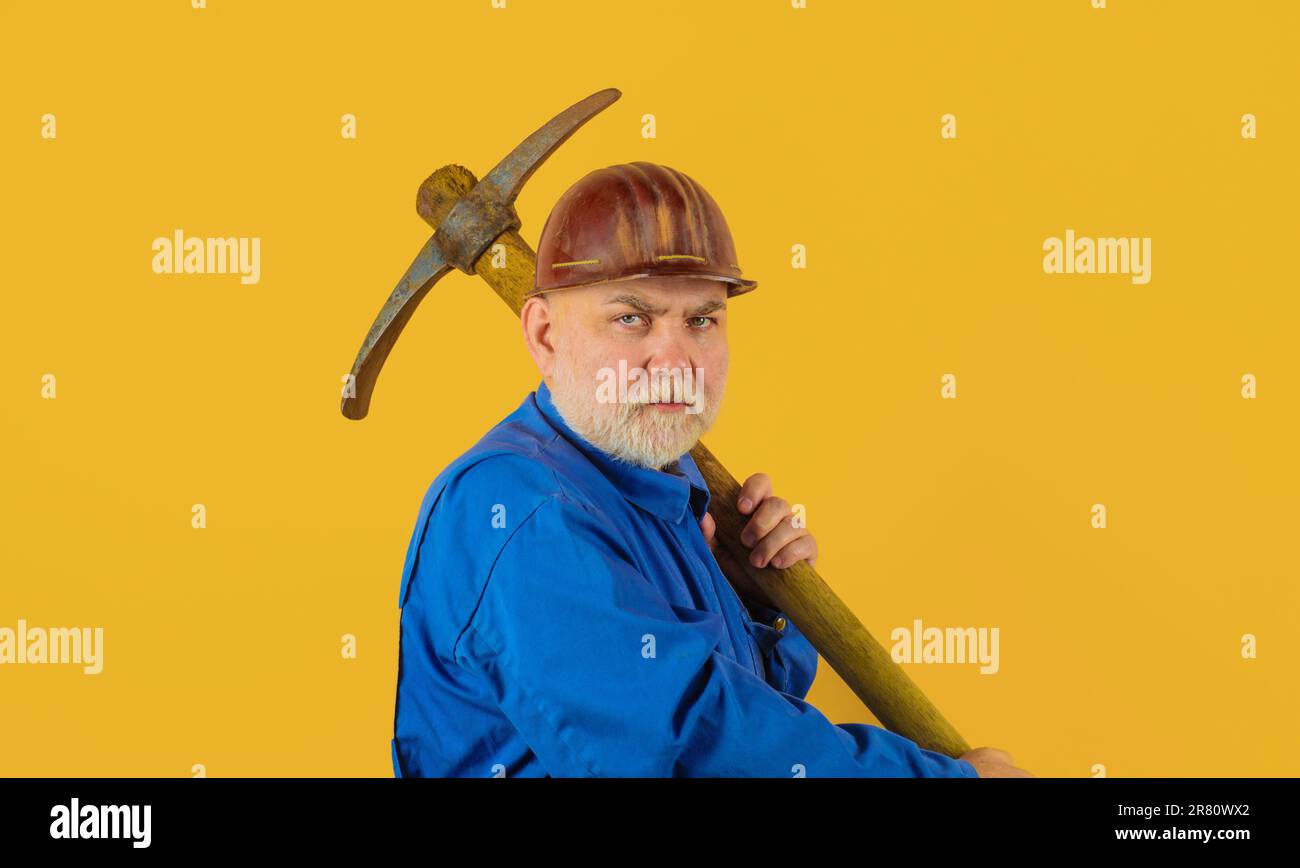 Bauarbeiter in Uniform mit Spitzhacke. Bergarbeiter mit Spitzhacke. Bergbauindustrie. Männlicher Arbeiter mit Bauwerkzeugen. Bärtiger Baumeister in Schutzhelm Stockfoto