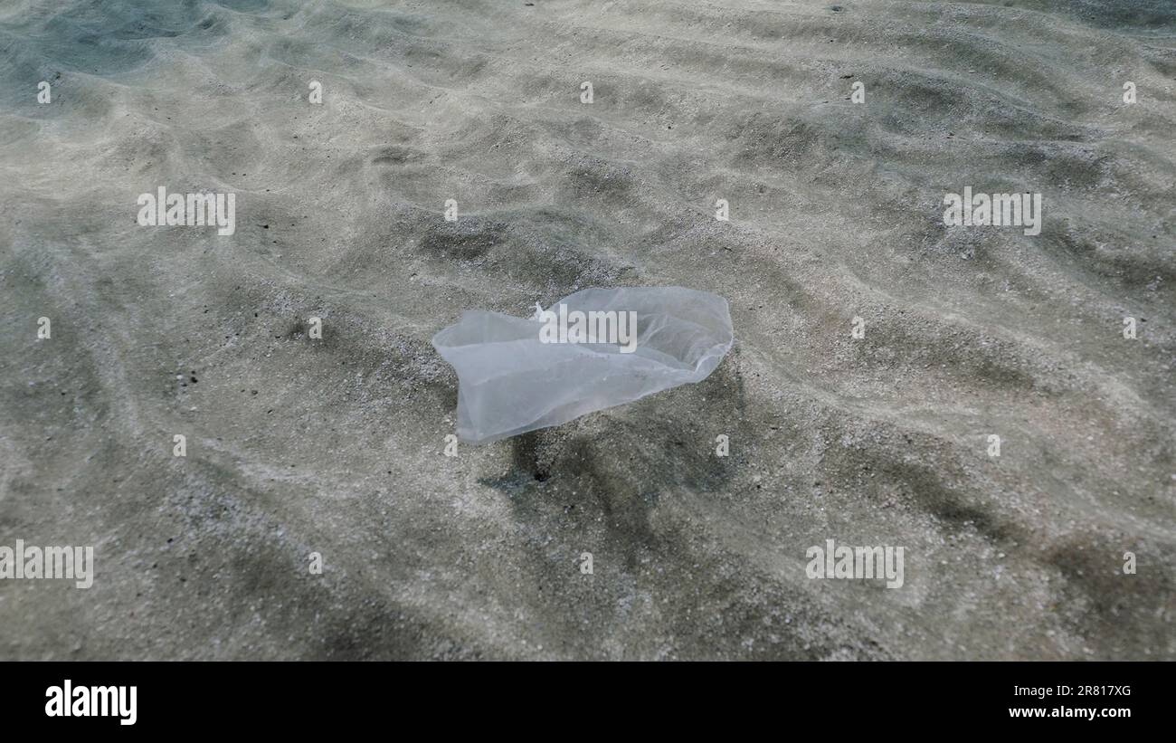 Plastikverschmutzung, weißer Plastikbeutel bewegt sich langsam im Wasserstrom über sandigen Boden Verschließen des sandigen Bodens in flachem Wasser mit Plastikbeutel, Rot Stockfoto