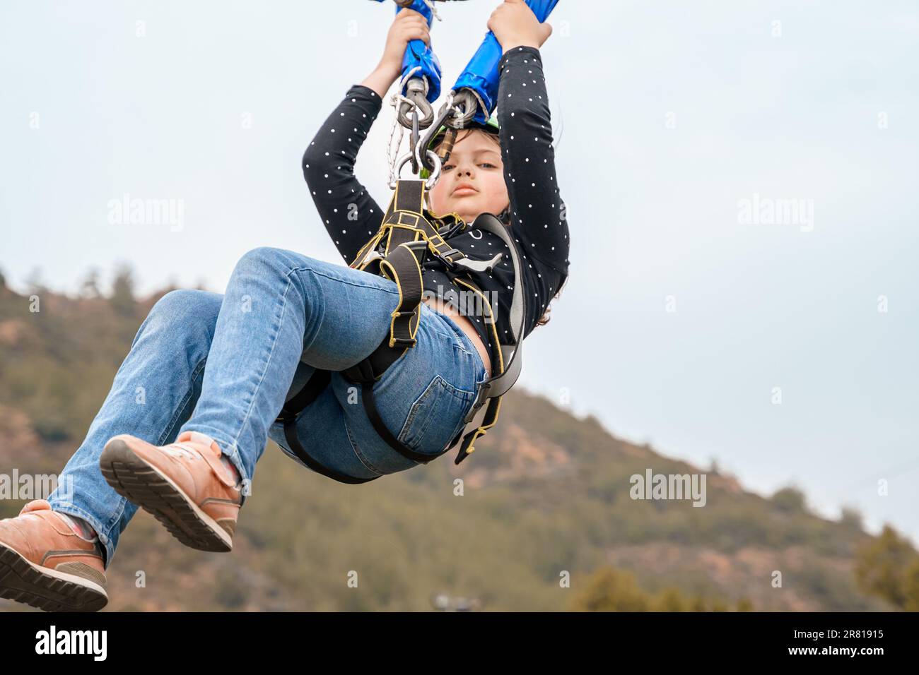 Teenager Mädchen Bungee fliegt im Seilpark. Klettergeschirr Ausrüstung, grüner Sportschutzhelm. Hindernislauf zum Aufhängen. Kinder Kinder Stockfoto