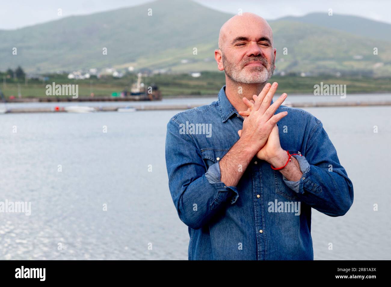 Großer, kahlköpfiger Mann, der mit dem Meer dahinter meditiert Stockfoto
