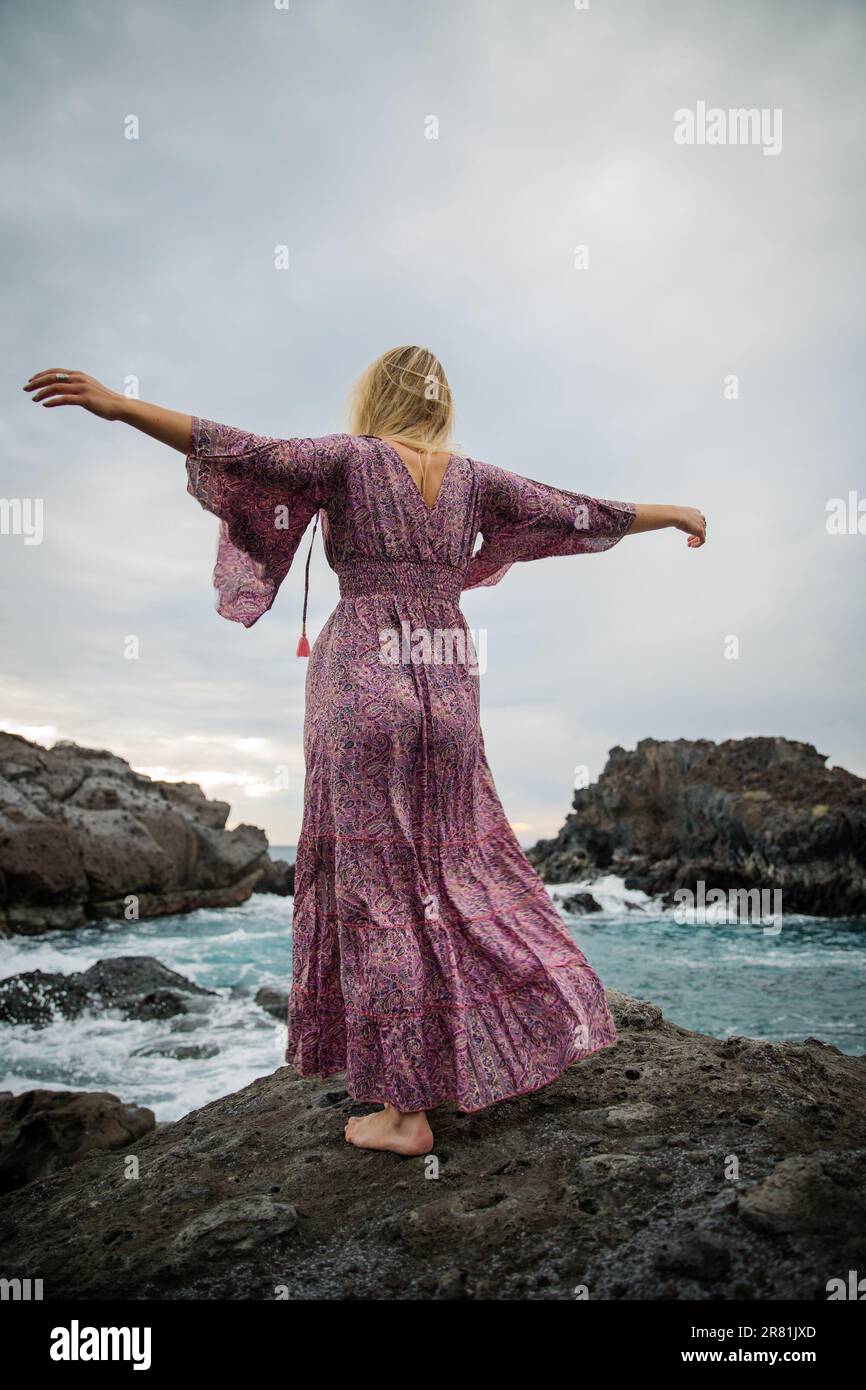 Eine Frau mit ausgestreckten Armen vervollständigt den Ozean und entspannt sich, Foto von hinten Stockfoto