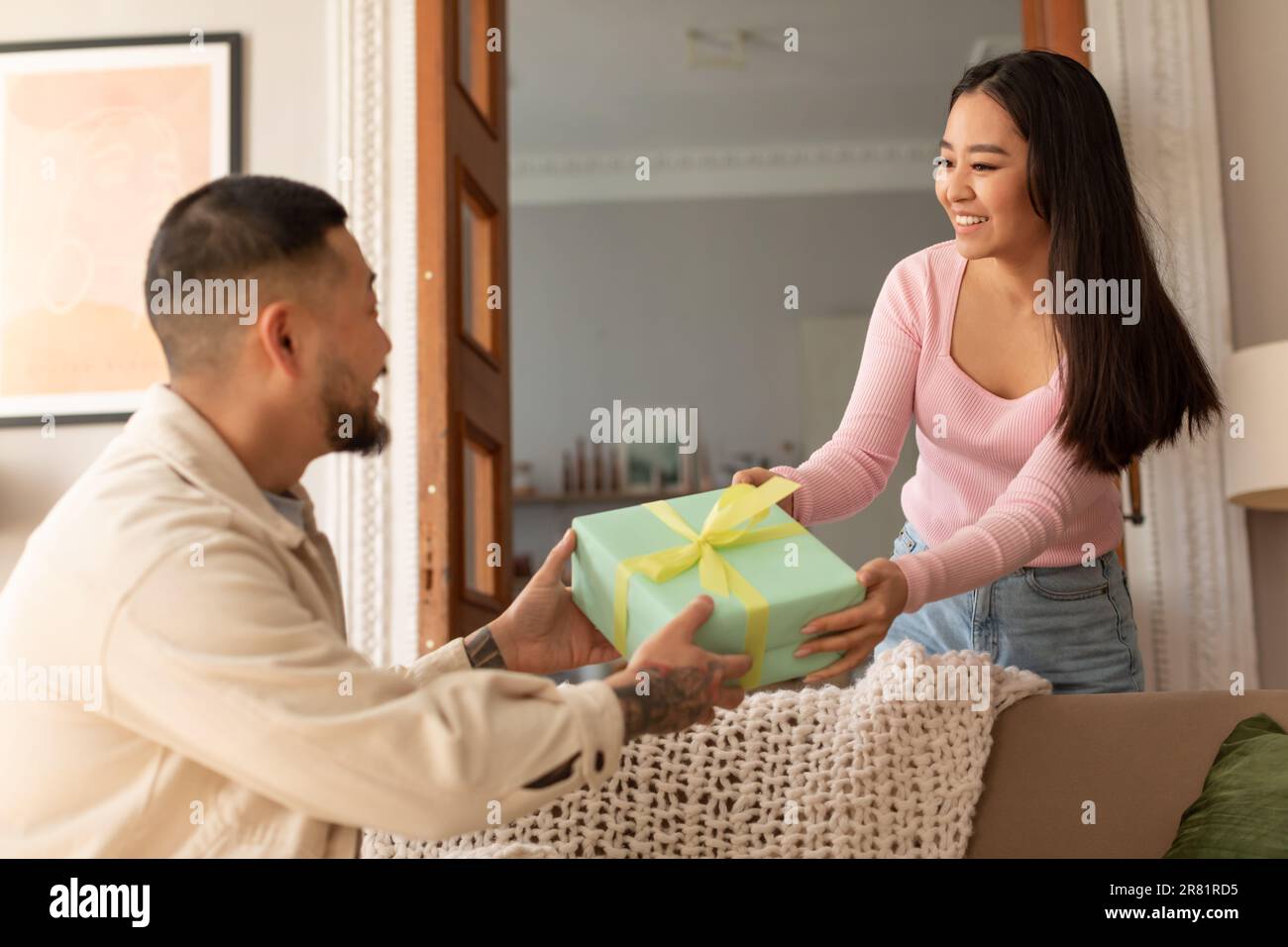 Eine Asiatin, die einem Mann im Wohnzimmer eine Geschenkbox schenkt Stockfoto