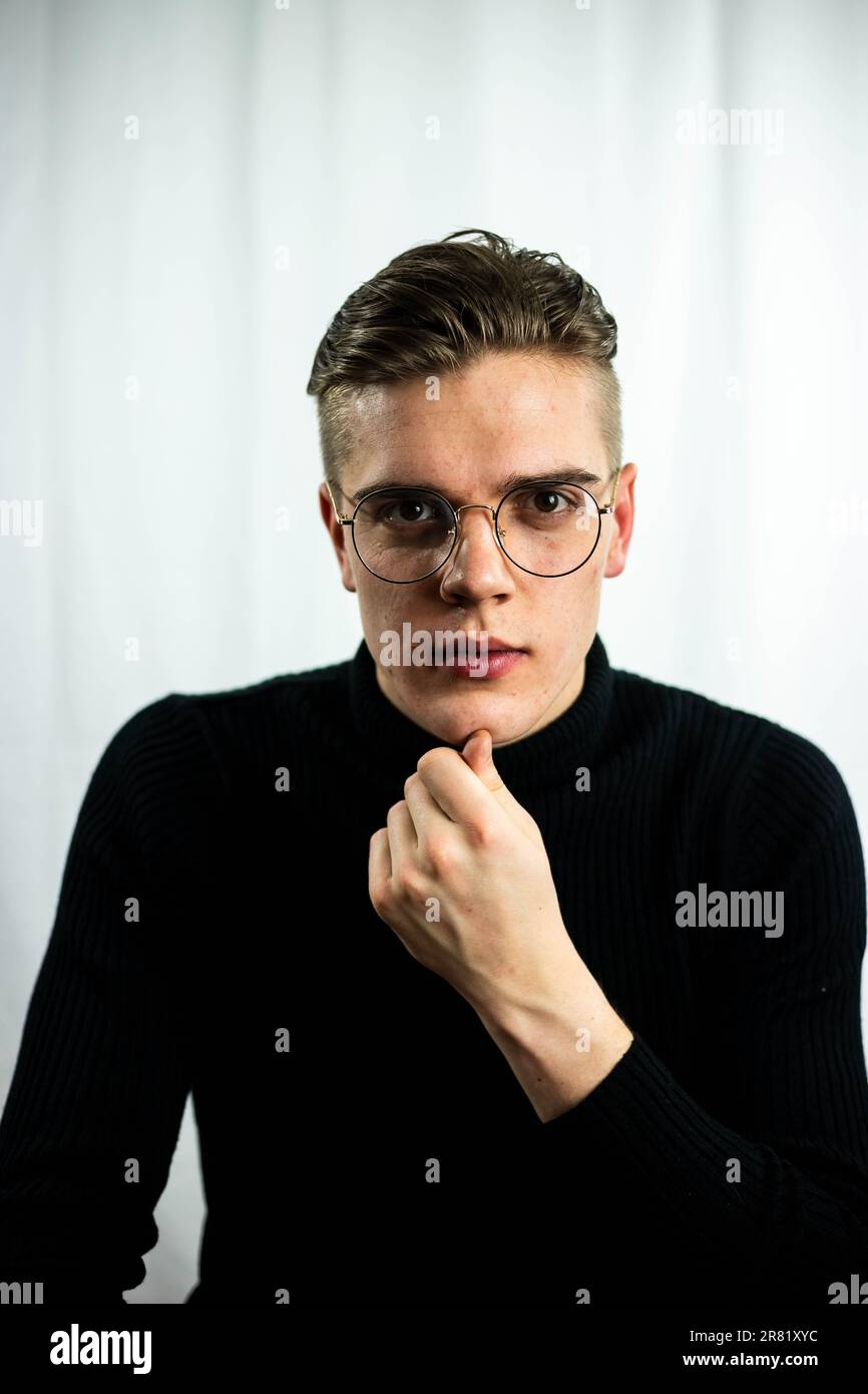 Ein Erwachsener mit schwarzem Rollkragenpullover und einer Brille steht vor einem grauen Hintergrund Stockfoto