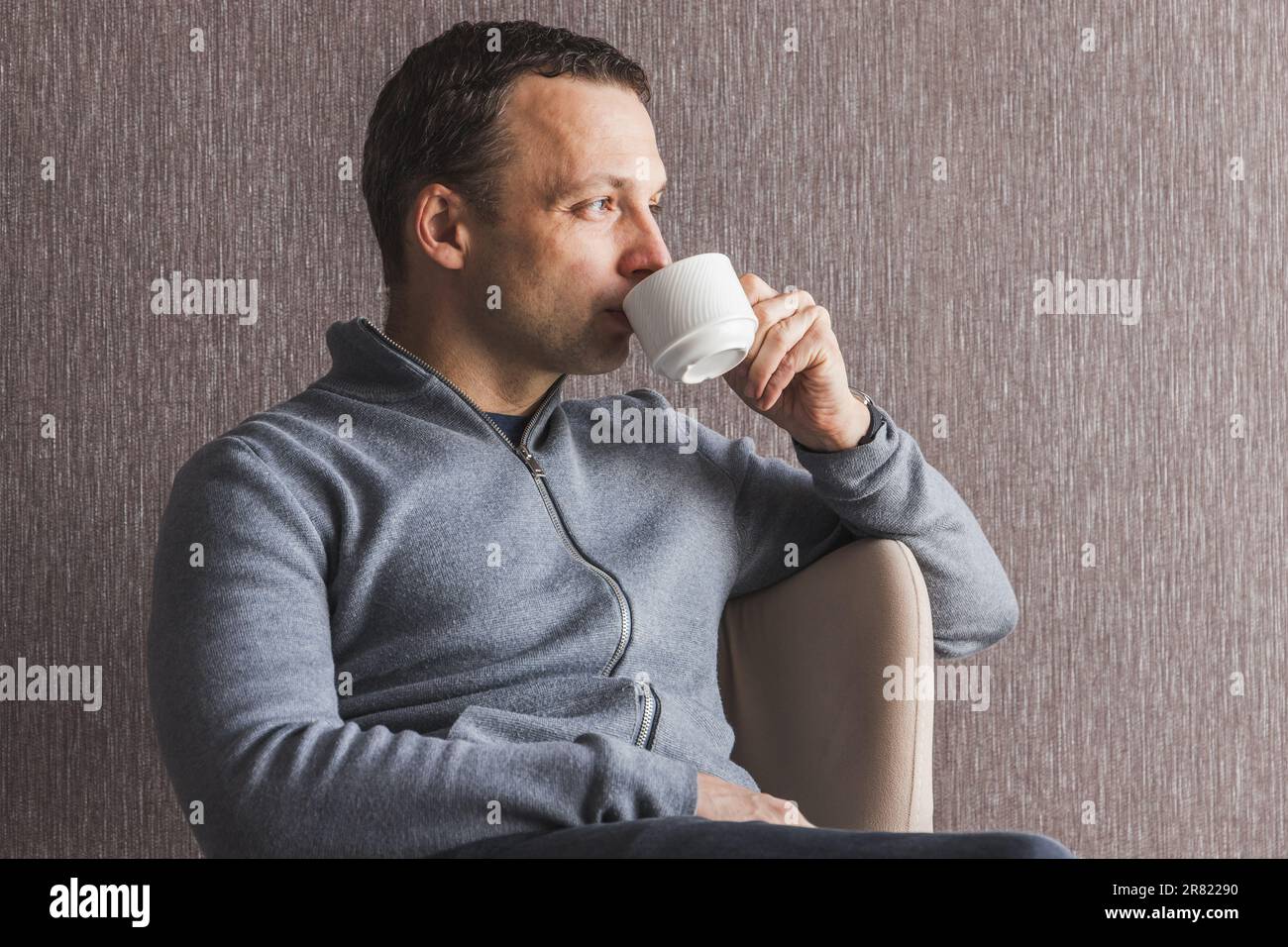 Junger erwachsener osteuropäischer Mann trinkt Kaffee im Sessel, Studiofoto Stockfoto