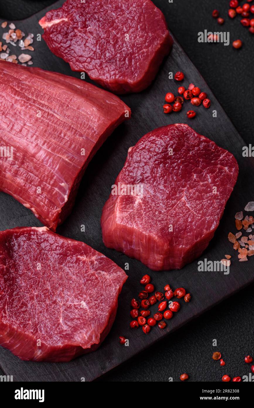 Saftiges rohes Rindfleisch mit Gewürzen, Salz und Kräutern auf dunklem ...