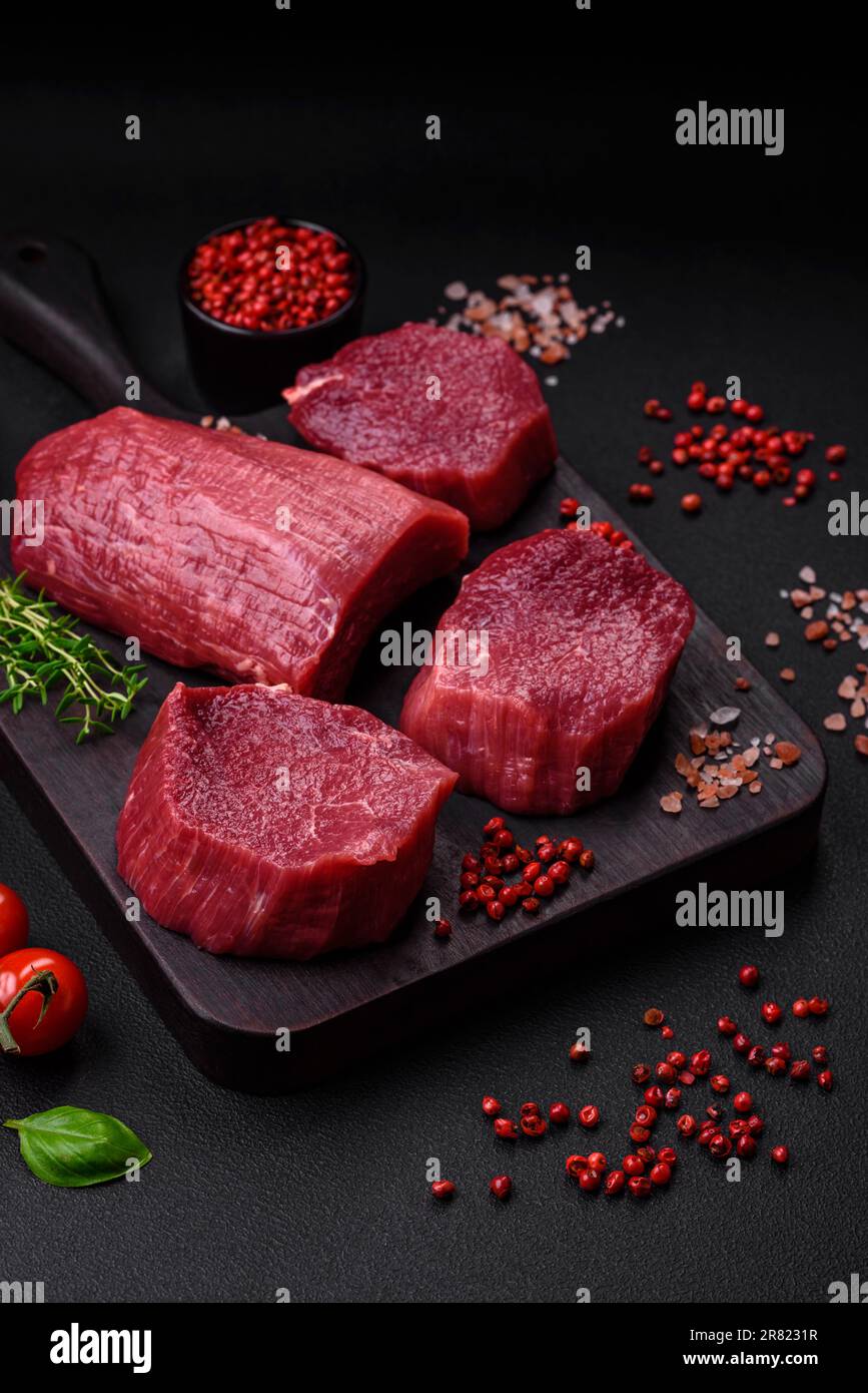 Saftiges rohes Rindfleisch mit Gewürzen, Salz und Kräutern auf dunklem Betonhintergrund