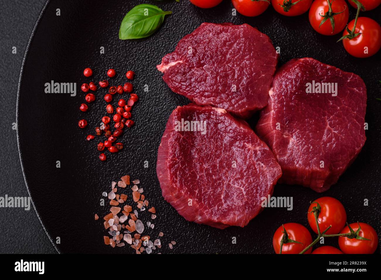Saftiges rohes Rindfleisch mit Gewürzen, Salz und Kräutern auf dunklem ...