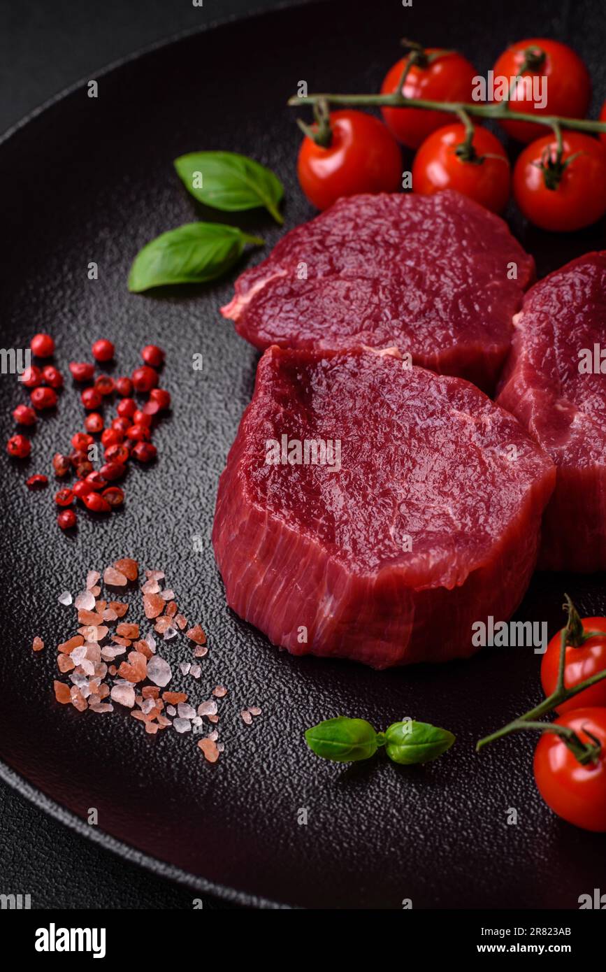 Saftiges rohes Rindfleisch mit Gewürzen, Salz und Kräutern auf dunklem ...