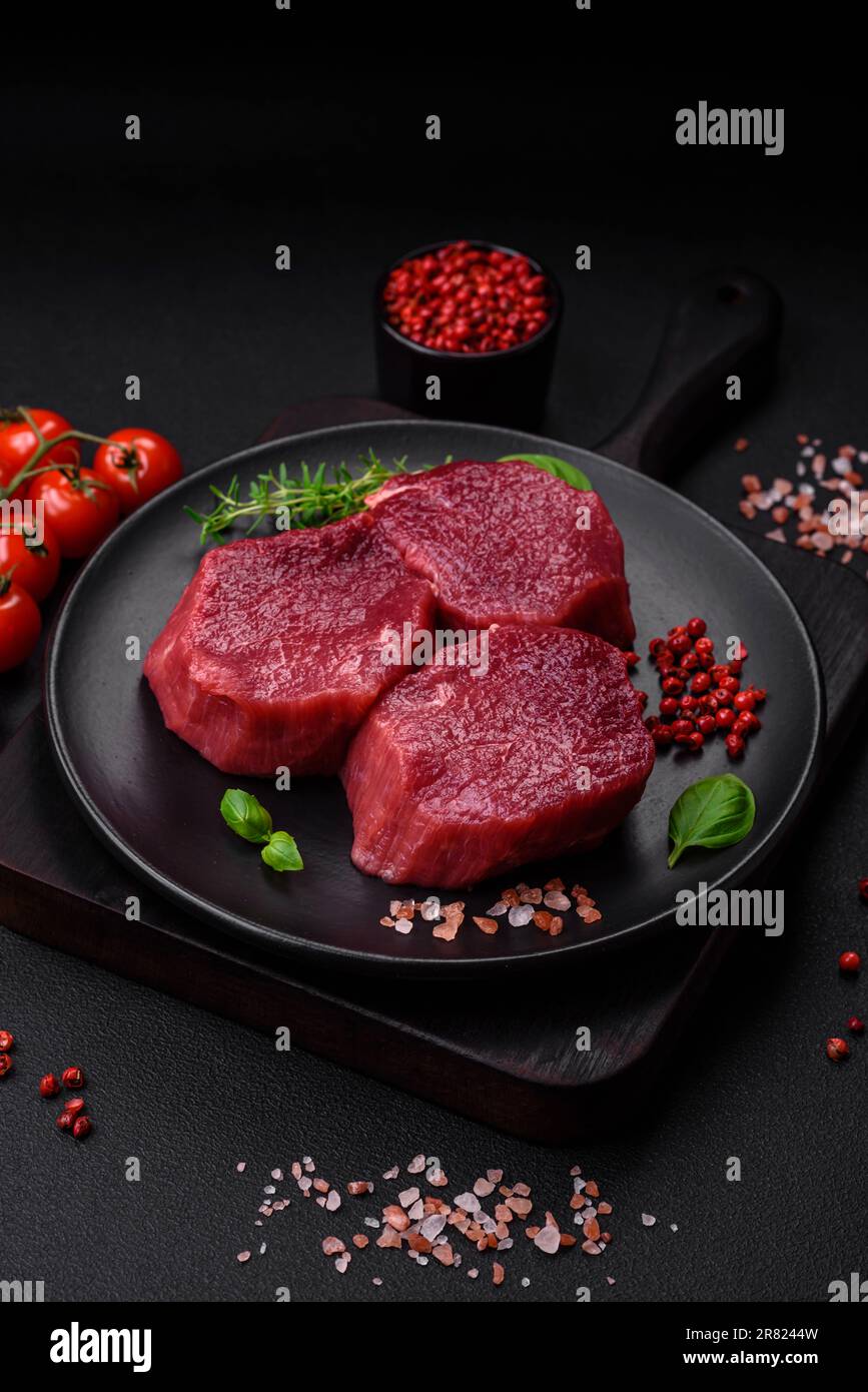 Saftiges rohes Rindfleisch mit Gewürzen, Salz und Kräutern auf dunklem ...