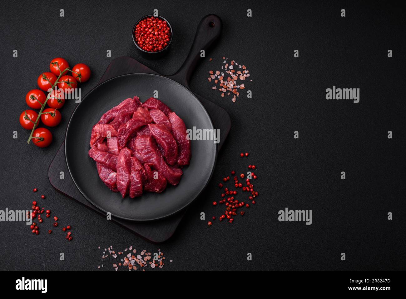 Saftiges rohes Rindfleisch mit Gewürzen, Salz und Kräutern auf dunklem ...