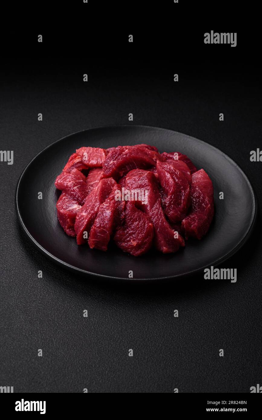 Saftiges rohes Rindfleisch mit Gewürzen, Salz und Kräutern auf dunklem ...