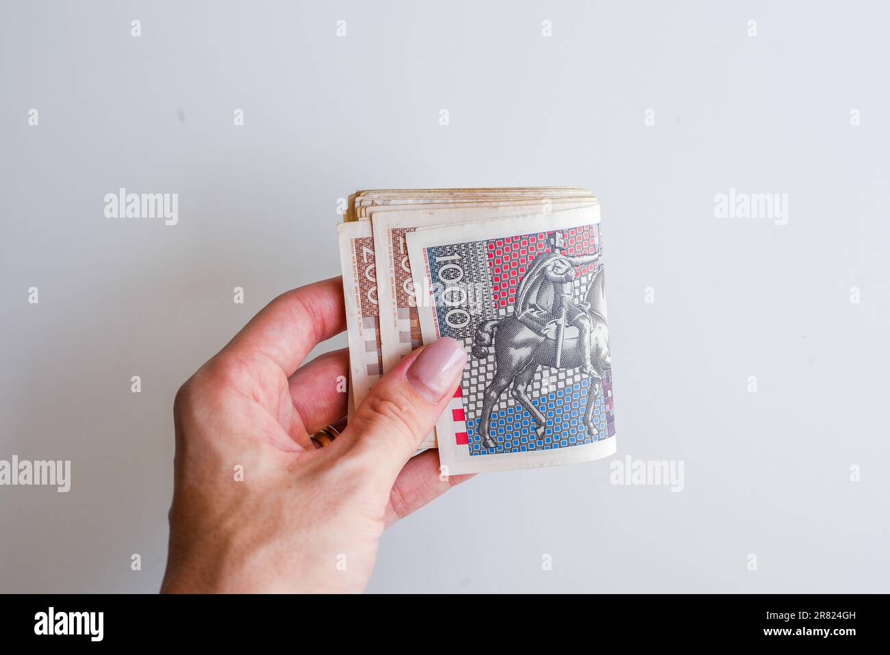 Eine Hand ist abgebildet, die ein Deck mit Dollarscheinen vor einem neutralen Hintergrund hält Stockfoto