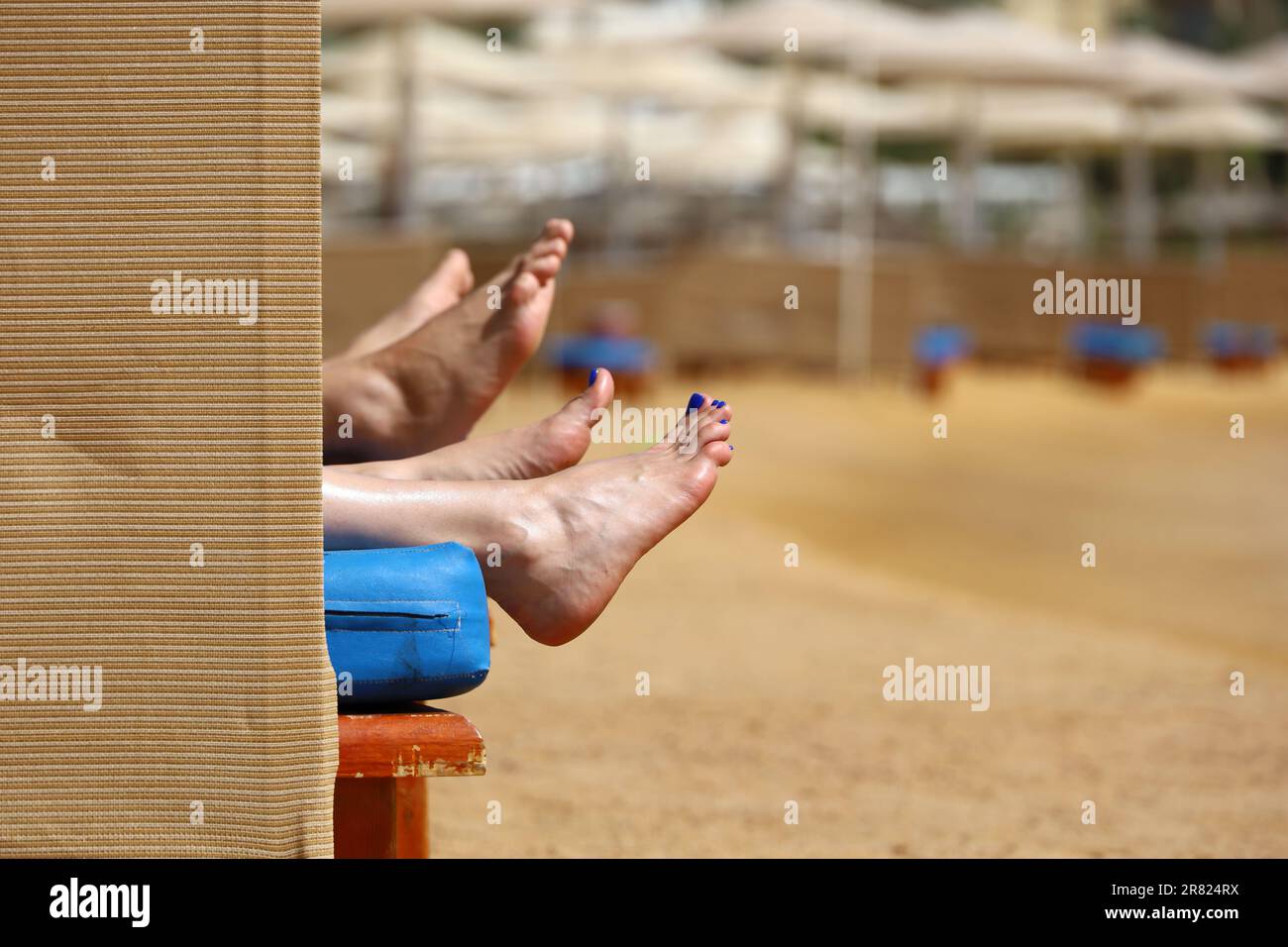 Ein paar Sonnenbräuner im Liegestuhl im Sea Resort. Weibliche und männliche Füße an einem Sandstrand Stockfoto